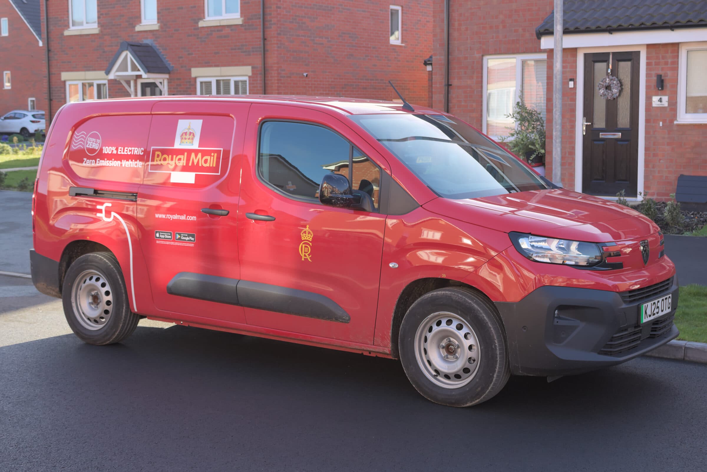 A red Royal Mail electric delivery van on a British residential street